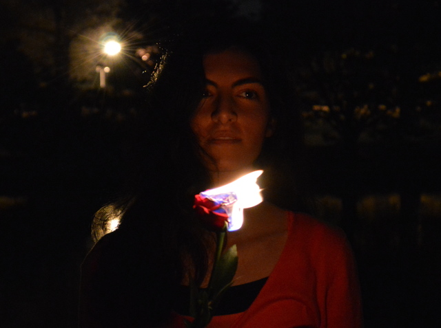 Maryam's face lit by a burning rose while she sits